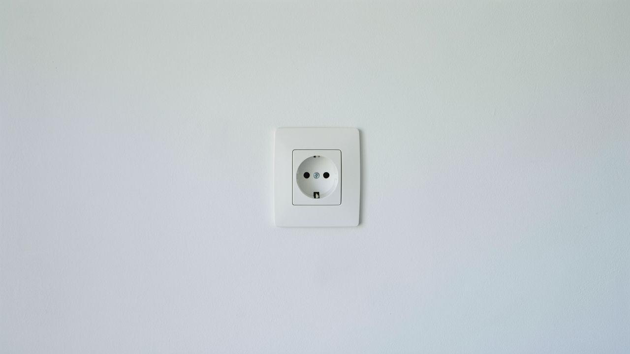 Eine leere Steckdose an einer hellen Wand — das Kabel ist gezogen.